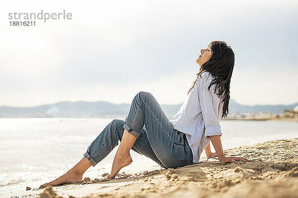 Frau mit geschlossenen Augen entspannt sich im Sand am Strand