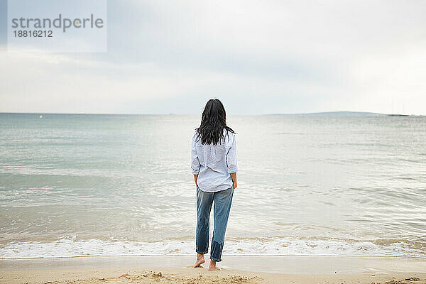 Frau mit Händen in Taschen und Blick aufs Meer