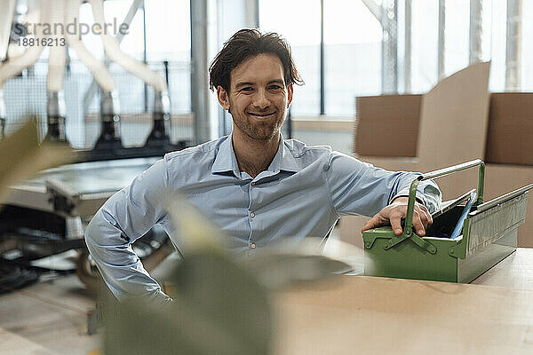 Happy young businessman with toolbox in factory