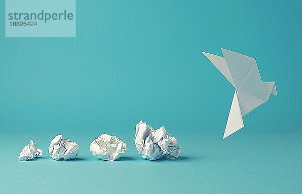 Zerknitterte Papierkugeln mit einer Origami Papiertaube  Frieden  Freiheit oder Gelegenheit Konzept auf einem blaün Hintergrund