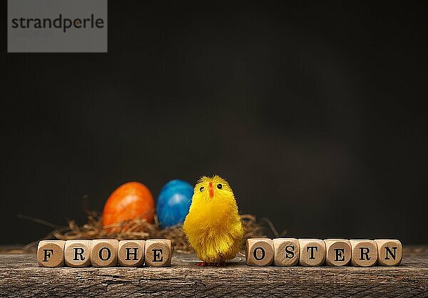 Ostern Hintergrund mit einem niedlichen Huhn und das deutsche Wort Frohe Ostern auf Holzwürfel auf einem alten rustikalen Holztisch