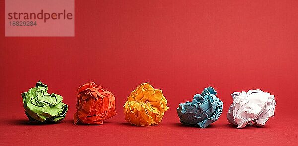 Bunte zerknüllte Papierkugeln auf rotem Studiohintergrund  Kreativität oder Diversitätskonzept  tolle Ideen  Teamarbeit
