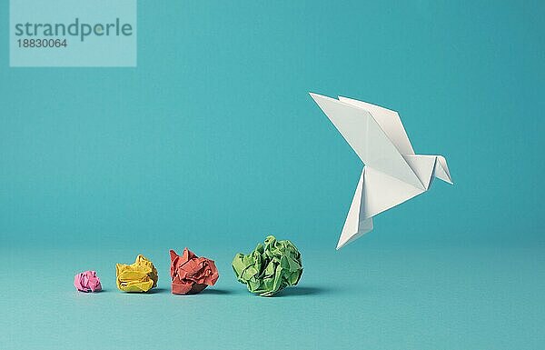 Bunte zerknitterte Papierkugeln mit einer Origami Papiertaube  Frieden  Freiheit  Vielfalt oder Gelegenheit Konzept auf einem blaün Hintergrund