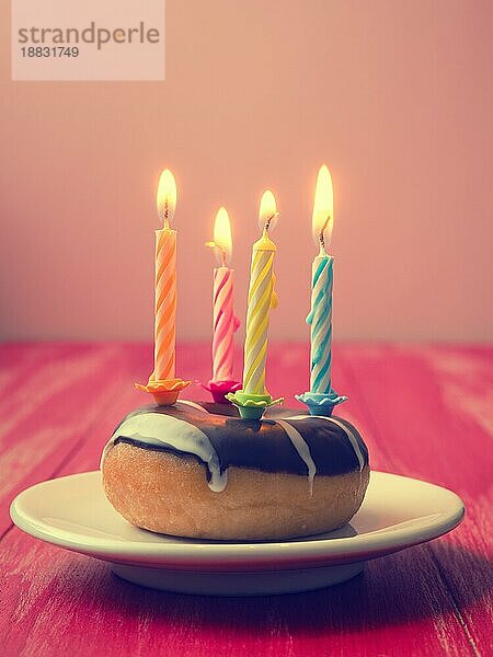 Bunte Geburtstagskerzen mit einem Donut auf einem roten Holztisch  Vintage Farbe stilisiert