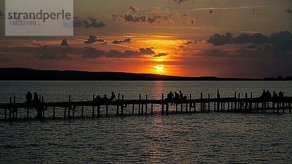 Gruppe von nicht erkennbaren Menschen in Silhouette sitzen auf Steg Pier beobachten Sonnenuntergang Sonnenuntergang am Steinhuder Meer in Deutschland