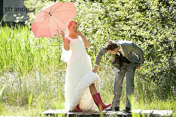 braut und bräutigam mit regenschirm und gummistiefel