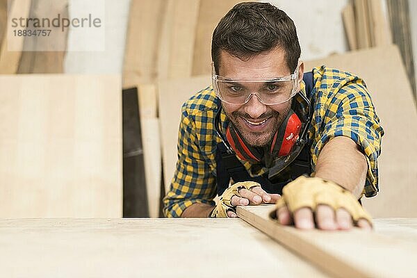 Glücklicher männlicher Schreiner  der Holzbretter in der Werkstatt zurechtrückt