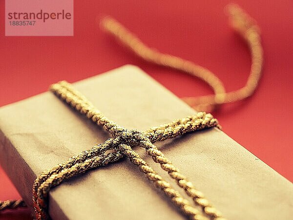 Ein Weihnachtsgeschenk mit goldener Geschenkbank auf rotem Hintergrund  selektiver Fokus auf den Vordergrund