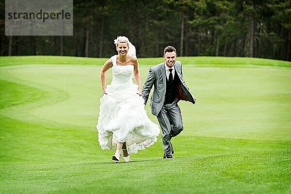 Braut und Bräutigam laufen auf dem grünen Gras