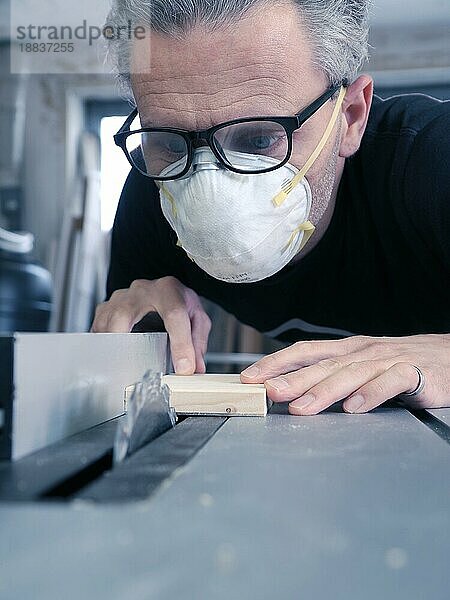Mann mit Staubmaske und Schutzbrille bei der Arbeit an einer Kreissäge  Arbeitsschutzkonzept