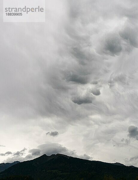 Abstrakte ungewöhnlichen bewölkten Himmel Hintergrund in milchig grau und weiß und einem dunklen Berg Silhouette