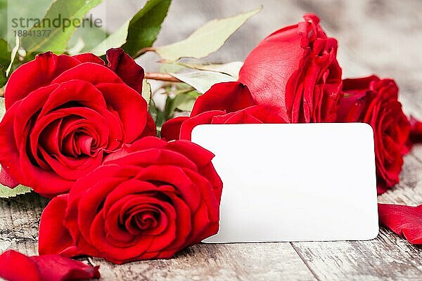 Rote Rosen mit einem leeren Geschenkanhänger auf einer Holzkrone