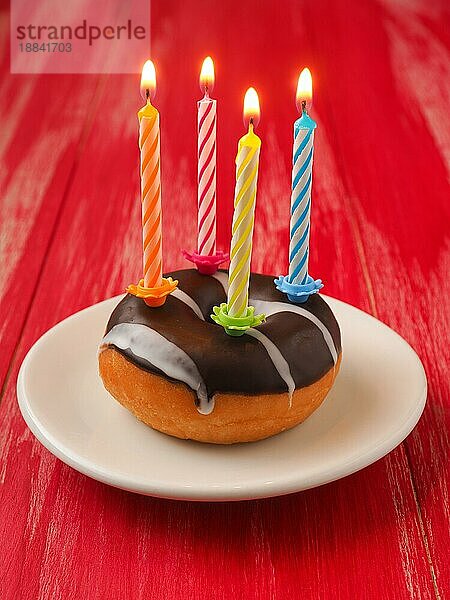 Bunte Geburtstagskerzen mit einem Donut auf einem roten Holztisch