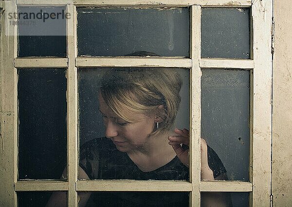 Portrait einer blonden Frau hinter altem Fenster