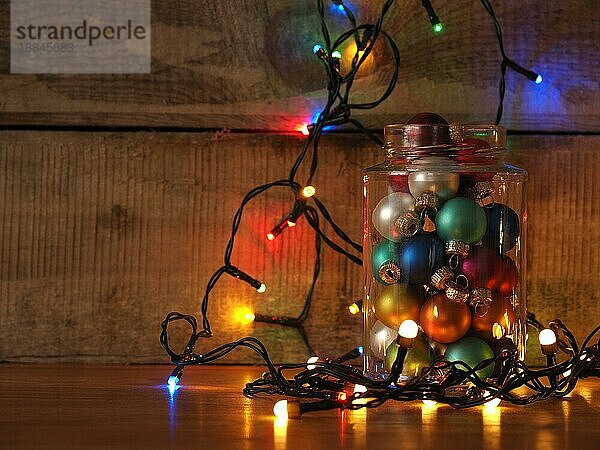 Ein mit Weihnachtskugeln gefülltes und mit bunten Lichterketten dekoriertes Bonbonglas  saisonaler oder weihnachtlicher Hintergrund  Platz für Text