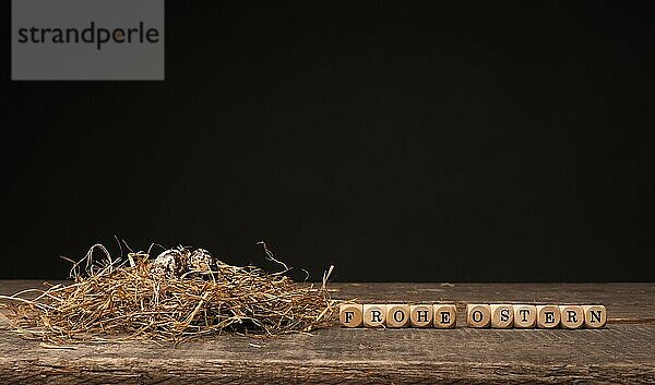 Osterkonzept mit kleinen Eiern in einem natürlichen Nest auf Holz  deutsche Worte Frohe Ostern auf Holzwürfeln