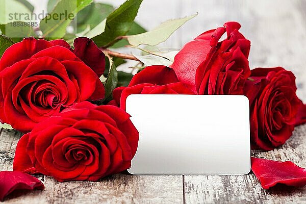 Rote Rosen mit einem leeren Geschenkanhänger auf einer Holzkrone