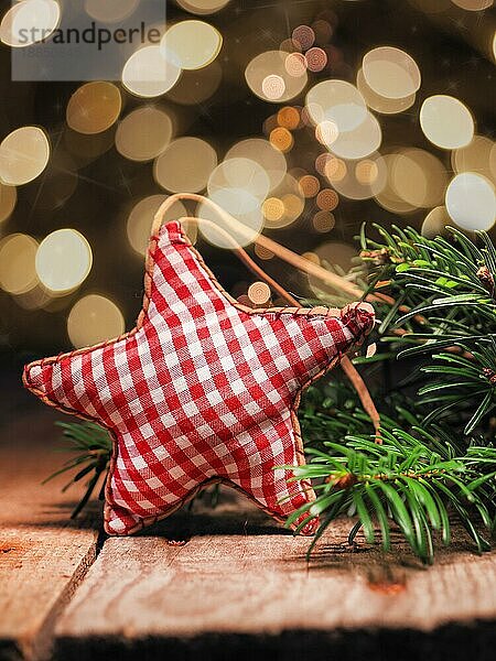 Selbstgemachter Stoffstern mit Tannenzweigen auf einem Holztisch vor einem Weihnachtsbaum Bokeh. Saisonale oder Weihnachten Hintergrund