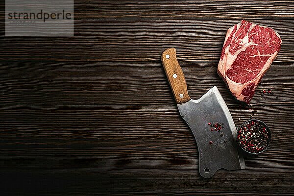 Draufsicht auf rohes frisch marmoriertes Fleisch Steak Ribeye  rustikales Fleischbeil  Gewürze auf hölzernem Hintergrund mit Platz für Text. Kochen saftig Bio-Steak Metzgerei Konzept  gesunde saubere Ernährung  Nahaufnahme