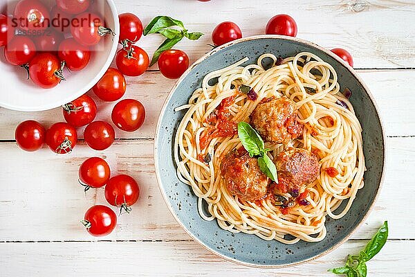 Nahaufnahme von leckeren Spaghetti mit Fleischbällchen und Tomatensauce auf einem Teller. Serviert auf einem weißen  rustikalen Holztisch. Ein italienisch-amerikanisches Gericht. Ansicht von oben. Selektiver Fokus