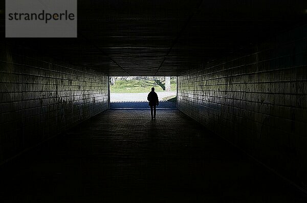 Silhouette einer Person  die durch eine dunkle Unterführung geht und das Licht am Ende des Tunnels symbolisiert