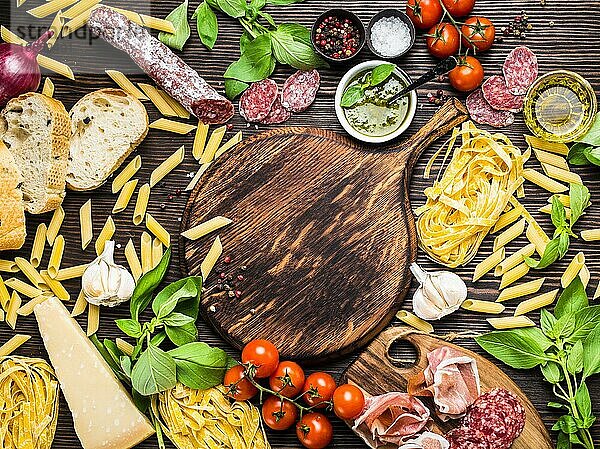 Draufsicht auf italienische traditionelle Lebensmittel  Vorspeisen und Snacks wie Salami  Prosciutto  Käse  Pesto  Ciabatta  Olivenöl  Pasta auf rustikalem Holzbrett mit Platz für Text in der Mitte