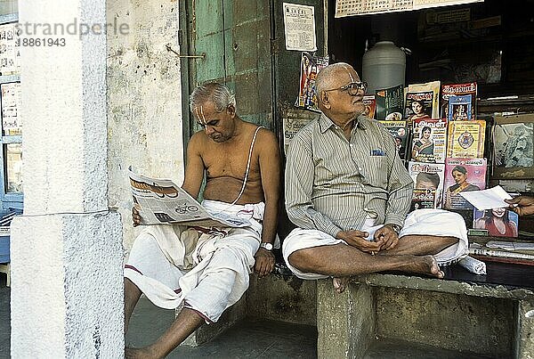 Ein alter Mann liest Zeitung und ein Mann sitzt vor einem kleinen Laden  Mylapore  Chennai  Tamil Nadu  Indien  Asien