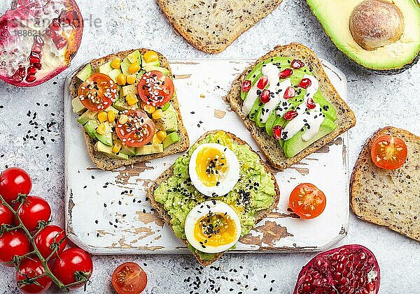 Avocado-Toasts mit Ei  Tomaten  Gewürze auf weißem Holz rustikalen Schneidebrett  Stein Hintergrund. Zutaten für gesunde Frühstücks-Avocado-Sandwiches mit verschiedenen Belägen  Draufsicht  Nahaufnahme