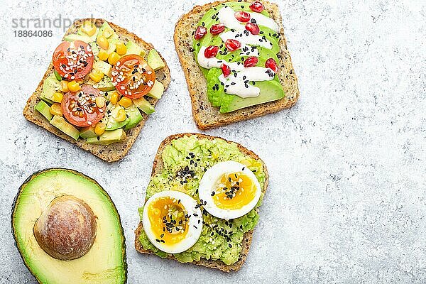 Avocado-Toasts mit Ei  Tomaten  Gewürzen und einer halben ganzen Avocado auf weißem Steinhintergrund. Gesunde Frühstücks-Avocado-Sandwiches mit verschiedenen Belägen  Draufsicht  Nahaufnahme