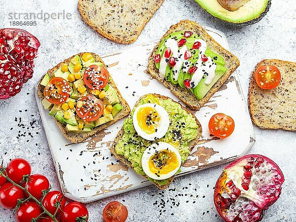 Avocado-Toasts mit Ei  Tomaten  Gewürze auf weißem Holz rustikalen Schneidebrett  Stein Hintergrund. Zutaten für gesunde Frühstücks-Avocado-Sandwiches mit verschiedenen Belägen  Draufsicht  Nahaufnahme