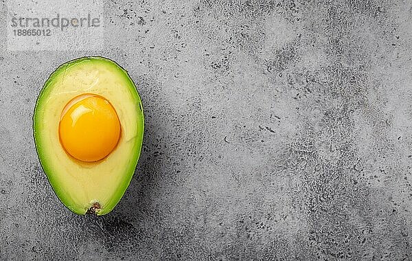 Lebensmittel reich an gesunden Fetten für eine ausgewogene Ernährung: rohes Eigelb in frisch geschnittene halbe Avocado auf grauem Stein Hintergrund. Ketogene Low-Carb-Diät oder Clean-Eating-Konzept  Draufsicht mit Platz für Text