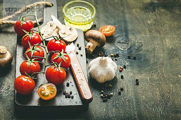 Kirschtomaten  Champignons auf Holzbrett  Messer. Mit Knoblauch  Olivenöl. Kochender Hintergrund. Platz für Text. Rohe Zutaten zum Kochen. Essen kochen. Selektiver Fokus. Lebensmittel-Hintergrund