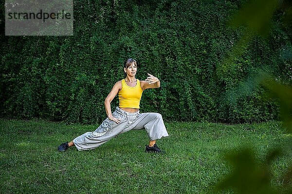 Eine Frau übt Tai Chi in einem Park. Das Üben im Freien bietet eine ruhige und entspannende Umgebung für Meditation und Konzentration