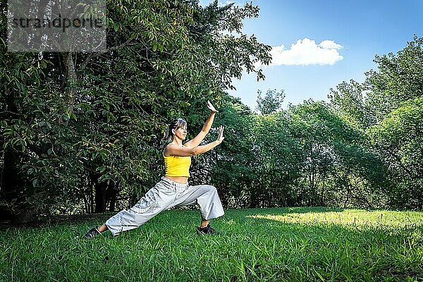 Gelassene erwachsene Frau bei einer Qigong Übung im Park. Verbindung mit der Natur und der Lebensenergie des Universums