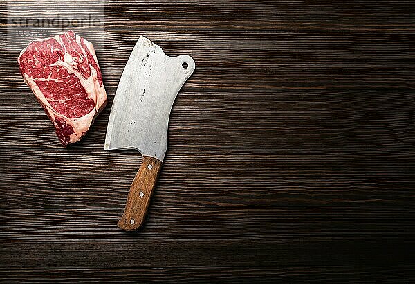 Draufsicht auf rohes  frisch marmoriertes Fleisch Steak Ribeye mit rustikalem Fleischbeil auf hölzernem Hintergrund mit Platz für Text. Kochen saftige Bio-Steak oder Metzgerei Konzept  gesunde saubere Ernährung  Nahaufnahme