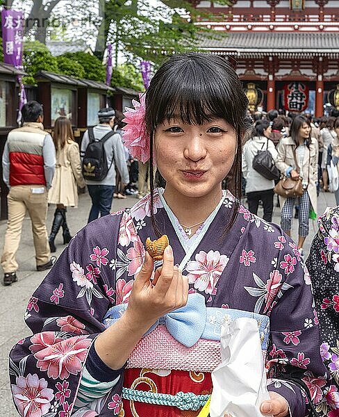 Tokio Japan. Ein Mädchen probiert Süßigkeiten in den Straßen von Asakusa