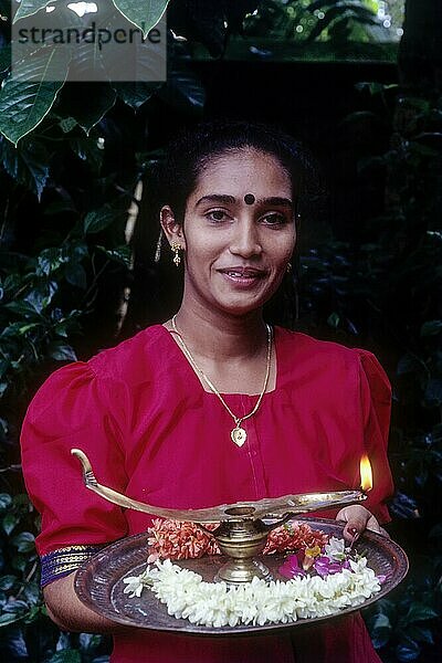 Ein Mädchen hält eine Öllampe und Blumen auf einem Tablett während des Onam-Festes  Kerala  Südindien  Indien  Asien