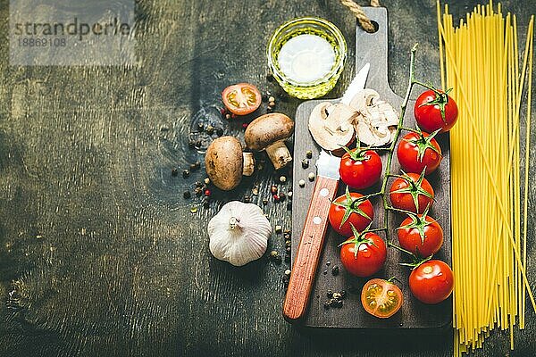 Kirschtomaten  Champignons  Spaghetti  Holzbrett  Messer. Knoblauch  Olivenöl. Kochender Hintergrund. Platz für Text. Zutaten zum Kochen. Kochendes Abendessen. Selektiver Fokus. Lebensmittel-Hintergrund