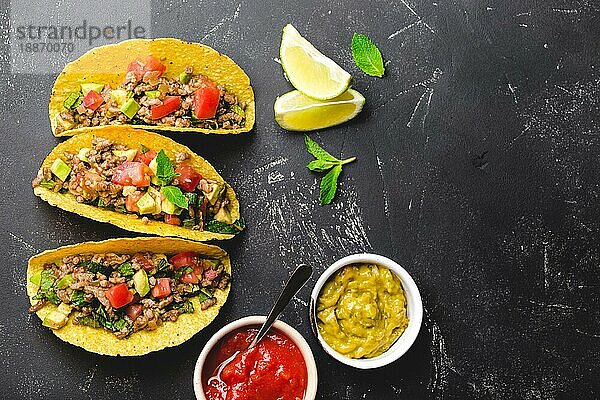 Draufsicht auf mexikanische Tacos mit Fleisch  Gemüse in gelber Maistortilla  serviert mit Salsa- und Guacamole-Saucen auf schwarzem rustikalem Steinhintergrund  Kopierraum. Traditionelles mexikanisches Gericht für Mittagessen  Abendessen