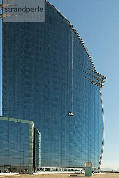 Arbeiter oder Fensterputzer auf einer Schaukelbühne im W Barcelona Hotel in Barceloneta. Das Gebäude hat eine halbmondförmige Silhouette mit 29 Stockwerken und ist ein neues Wahrzeichen Barcelonas Das riesige W Barcelona Hotel direkt am Meer im Stadtteil Barceloneta Barcelona