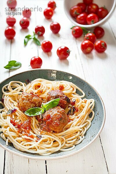 Nahaufnahme von leckeren Spaghetti mit Fleischbällchen und Tomatensauce auf einem Teller. Serviert auf einem weißen  rustikalen Holztisch. Ein italienisch-amerikanisches Gericht. Selektiver Fokus