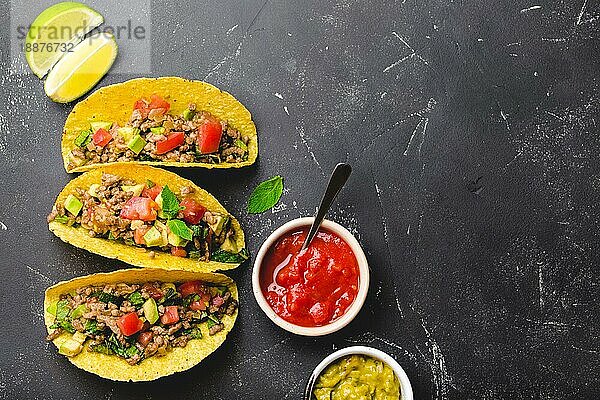 Draufsicht auf mexikanische Tacos mit Fleisch  Gemüse in gelber Maistortilla  serviert mit Salsa- und Guacamole-Saucen auf schwarzem rustikalem Steinhintergrund  Kopierraum. Traditionelles mexikanisches Gericht für Mittagessen  Abendessen