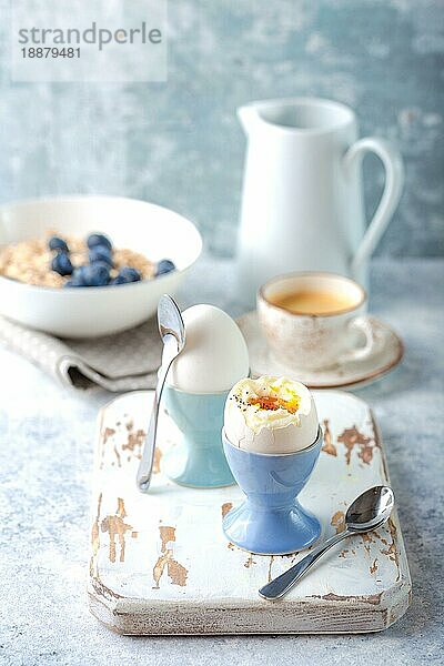 Frische weich gekochte Eier  Haferflocken mit Blaubeeren  Kaffeetasse  Milchkännchen. Weißer Beton rustikalen Hintergrund. Weiche Eier  gesundes Frühstück. Selektiver Fokus. Leckeres leichtes Fitness-Frühstückskonzept. Nahaufnahme