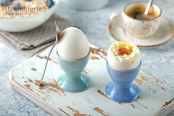 Frische weich gekochte Eier  Haferflocken mit Blaubeeren  Kaffeetasse  Milchkännchen. Weißer Beton rustikalen Hintergrund. Weiche Eier  gesundes Frühstück. Selektiver Fokus. Leckeres leichtes Fitness-Frühstückskonzept. Nahaufnahme