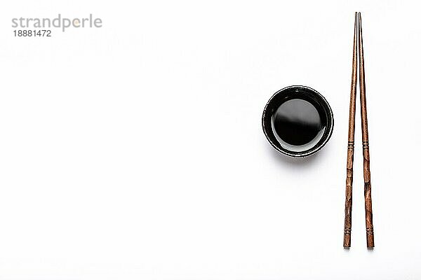Kleine rustikale Schüssel mit Sojasauce und hölzernen Essstäbchen auf weißem Hintergrund mit Platz für Text. Konzept des Sushi-Restaurants  japanische Küche oder Menüvorlage  Ansicht von oben