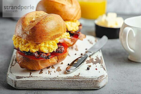 Frühstückssandwiches mit Rührei  Speck  Käse  Tomaten auf weißem Holzbrett  Glas mit frischem Orangensaft  weißer Hintergrund. Frühstück machen Konzept  selektiver Fokus