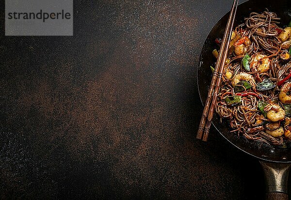 Nahaufnahme von chinesischen Soba-Rührnudeln mit Garnelen und Gemüse in einer alten  rustikalen Wokpfanne auf einem Betonhintergrund  Nahaufnahme  Draufsicht. Traditionelles asiatisches/thailändisches Gericht  Platz für Text