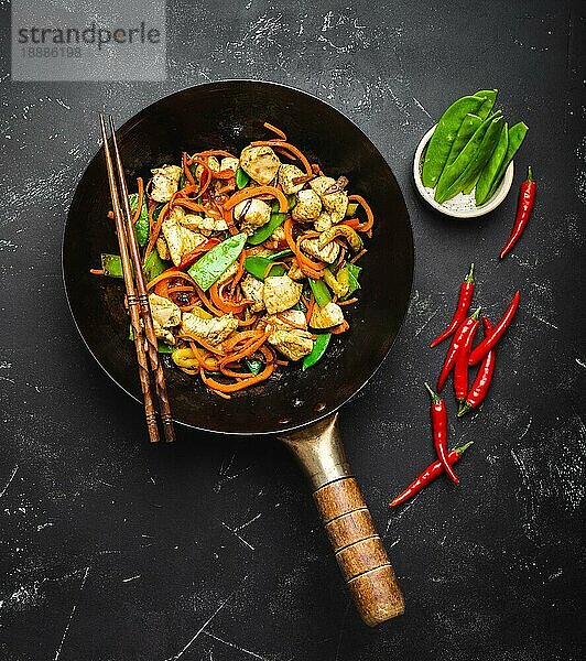 Gebratenes Huhn mit Gemüse in einer alten  rustikalen Wokpfanne  Stäbchen auf schwarzem Steinhintergrund  Nahaufnahme  Draufsicht. Traditionelle asiatische/thailändische Mahlzeit