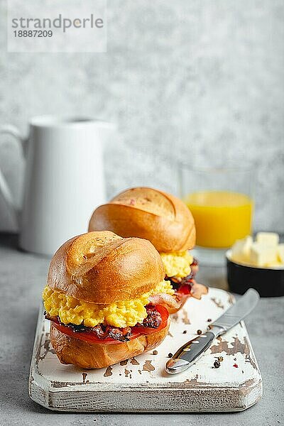 Frühstückssandwiches mit Rührei  Speck  Käse  Tomaten auf weißem Holzbrett  Glas mit frischem Orangensaft  weißer Hintergrund. Frühstück machen Konzept  selektiver Fokus