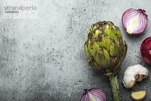 Lebensmittel Hintergrund mit freiem Raum für Text. Nahaufnahme  Draufsicht von geschnittenen rohen Zwiebeln  Knoblauch und ganze frische Artischocke auf rustikalem grauen Stein Hintergrund  Kochen  vegetarisches Essen oder gesunde Ernährung Konzept